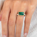 A rectangular emerald stone ring with a gold bezel and a sterling silver band, worn on a finger