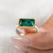 A rectangular emerald stone ring with a gold bezel and a sterling silver band, held in hand