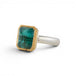 An emerald gemstone ring with a gold bezel and sterling silver band, on a white background