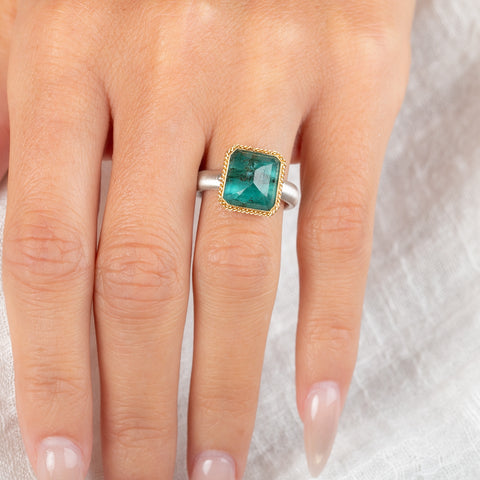 An emerald gemstone ring with a gold bezel and sterling silver band, worn on a hand