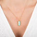 Gold necklace with a rectangular Ethiopian opal pendant on a person wearing a white top.