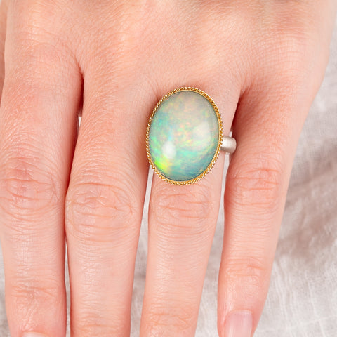 Hand wearing an Ethiopian opal ring with a gold bezel and sterling silver band