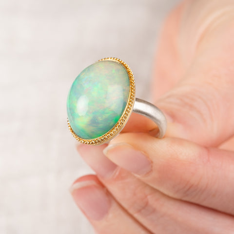 Hand holding an ethiopian opal ring with a gold bezel and sterling silver band