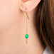 Gold drop earrings with teardrop-shaped opal gemstones and dangling chain accents, shown on a person's ear