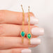 A pair of gold drop earrings with teardrop-shaped opal gemstones and dangling chain accents, held in hand.