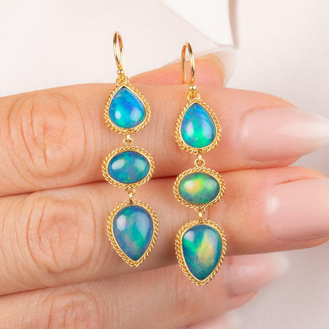Gold earrings featuring a trio of iridescent Ethiopian opal gemstones, held in hand.