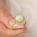 Gold ring featuring a circular Ethiopian opal gemstone set in a handmade 18k gold bezel, held in a hand.