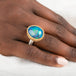 Gold and silver ring with an opal stone on a person's finger against a white background