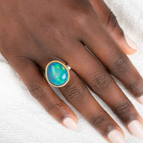 Gold and silver ring with an opal stone on a person's finger against a white background