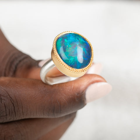 Gold and silver ring with an opal stone held in hand against a white background