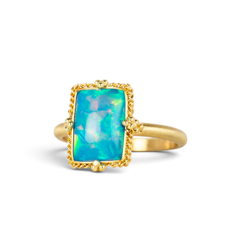 A handmade gold ring featuring an Ethiopian opal gemstone, against a white backdrop.