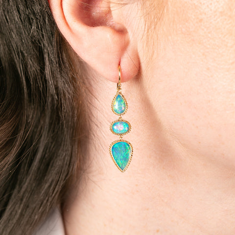 Close-up of an ear wearing a gold earring with australian opal gemstones.