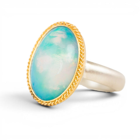 Ring with a gold bezel and silver band and a large Ethiopian opal gemstone on a white background