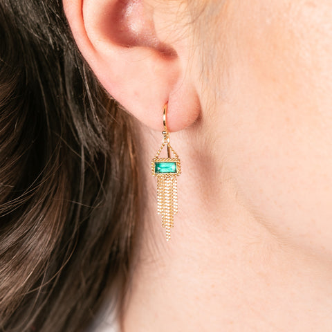 Gold earring with emerald gemstone worn by a person