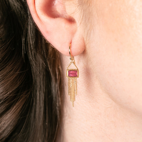 Gold earrings with tourmaline gemstones and gold chain tassels worn by a person