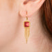 Gold earrings featuring fire opal gemstones and gold chain tassels, shown worn in a person's ear.