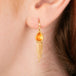 Gold earrings featuring vibrant orange fire opal gemstones, shown worn in a person's ear.