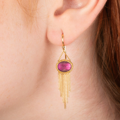 Gold earrings featuring vibrant pink  fluorite gemstones, shown worn on a person's ear.