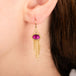 A gold dangle earring with oval pink fluorite gemstone and cascading chain tassel, shown worn on a model's ear.
