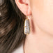 Gold earrings featuring fossilized coral gemstones worn by a person