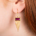 Gold earrings featuring rhodolite garnet gemstones, shown worn in a person's ear.