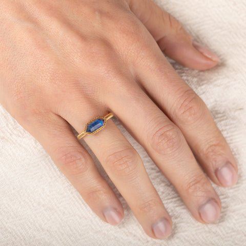 Gold ring with a moonstone on a person's finger against a white background
