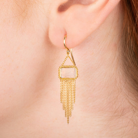 Gold earrings featuring moonstones and gold chain tassels, shown worn in a person's ear.