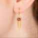 Gold earrings featuring oval rhodolite garnet gemstones, shown worn in a person's ear.
