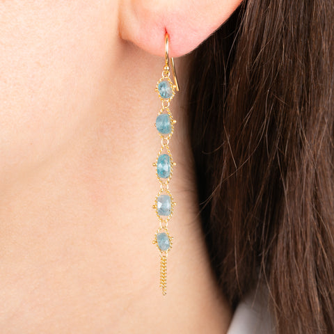 Gold earrings featuring a row of grandidierite stones, shown worn in a person's ear.