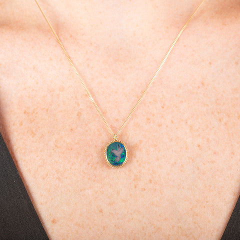 Handmade opal doublet pendant necklace featuring a carved hummingbird on a gold chain on a person