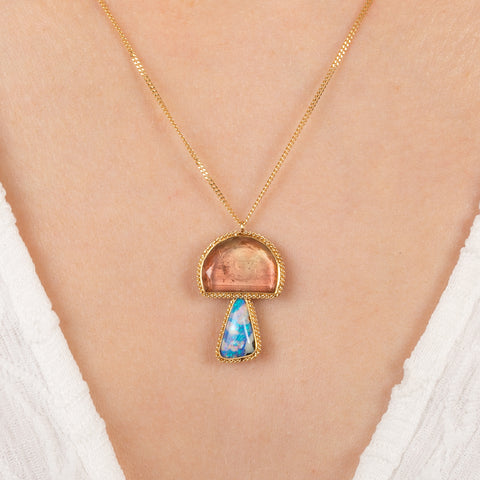Gold pendant with a mushroom design combining a tourmaline stone with a boulder opal stone on a person