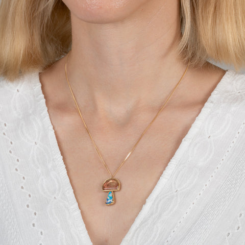 Gold pendant with a mushroom design combining a tourmaline stone with a boulder opal stone on a person