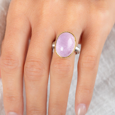 A ring featuring a large oval kunzite stone, set in a gold textured bezel with a sterling silver band, worn on a person's finger.