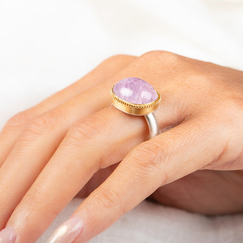 A gold and silver ring featuring a pink kunzite stone, worn on a person's finger