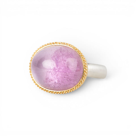 An oval kunzite ring with a gold bezel and sterling silver band, against a white background