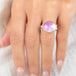 An oval kunzite ring with a gold bezel and sterling silver band, worn on a person's finger.
