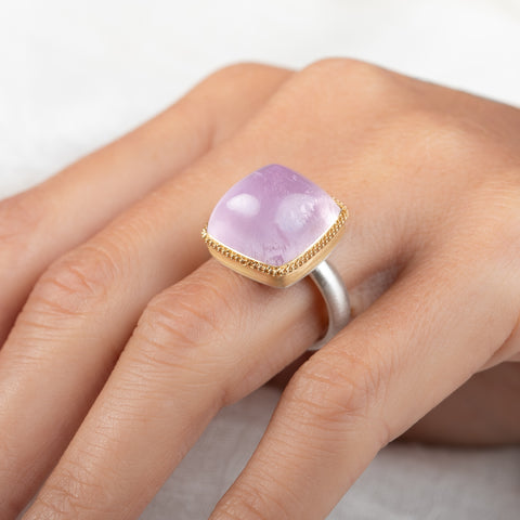 A square cushion-cut kunzite gemstone ring with a gold bezel and a sterling silver band, worn on a person's finger.