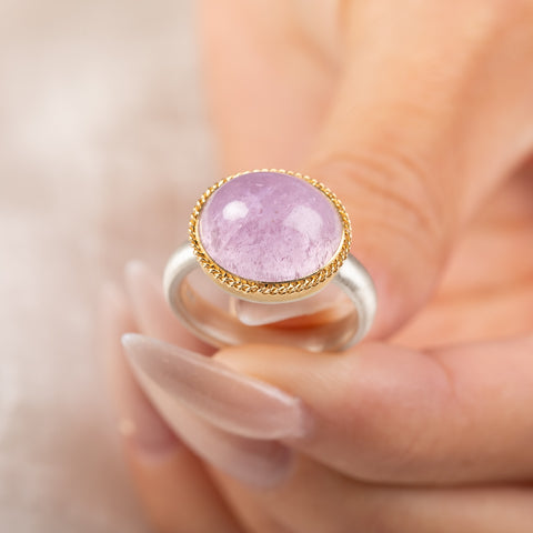 A gold and silver ring featuring a pink kunzite stone, held in hand.