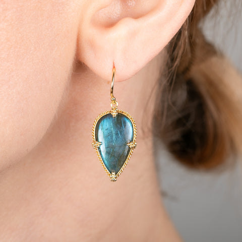 Teardrop-shaped labradorite gemstone earring with gold frame worn by a person.