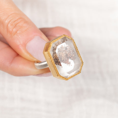 Gold and silver ring featuring a lodolite quartz stone held by a hand on a white background