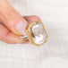 Gold and silver ring featuring a lodolite quartz stone held by a hand on a white background