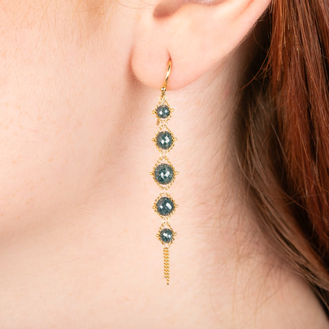 A gold earring featuring a row of shimmering blue diamonds, shown worn in a person's ear.