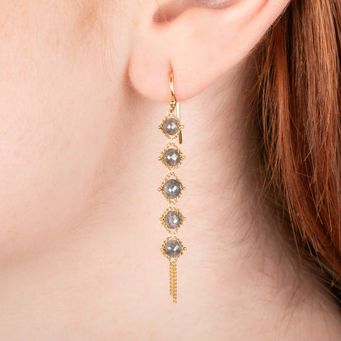 Gold earrings featuring five grey diamonds each, shown worn on a person's ear.