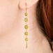 A gold earrings featuring a row of peridot gemstones, shown worn in a person's ear.