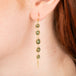 A gold earring featuring a row of green apatite gemstones, shown worn in a person's ear.