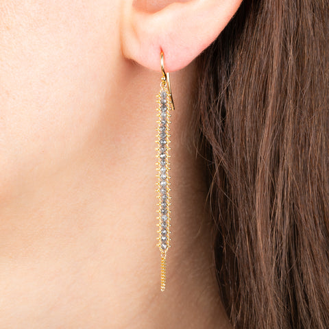 Gold earring featuring row of grey diamonds, worn on a person's ear.