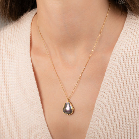 Gold necklace featuring a mabe pearl stone worn on a person's neck.