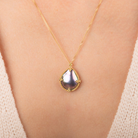 Gold necklace featuring a mabe pearl set in a handcrafted 18k gold bezel, worn on a person's neck.