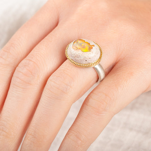 Close up of someone wearing a ring with a Mexican opal stone, gold bezel and sterling silver band on a white background