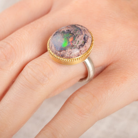 Close up of a person wearing a ring with a mexican opal stone and 18k gold bezel with a sterling silver band